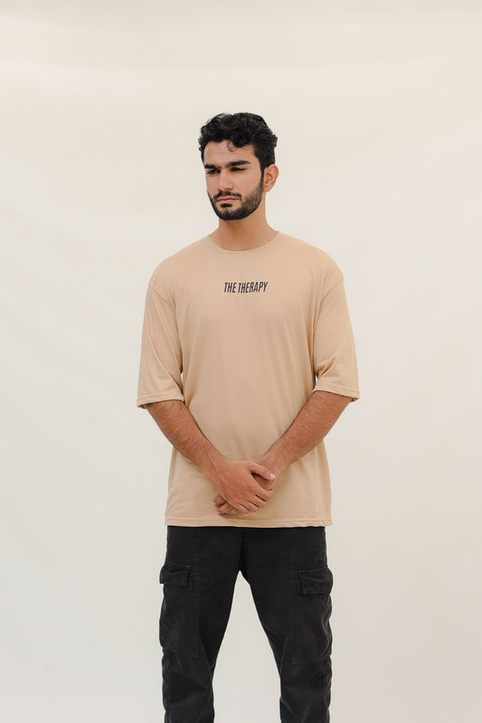 Man wearing a beige t-shirt with text and black pants on a white background