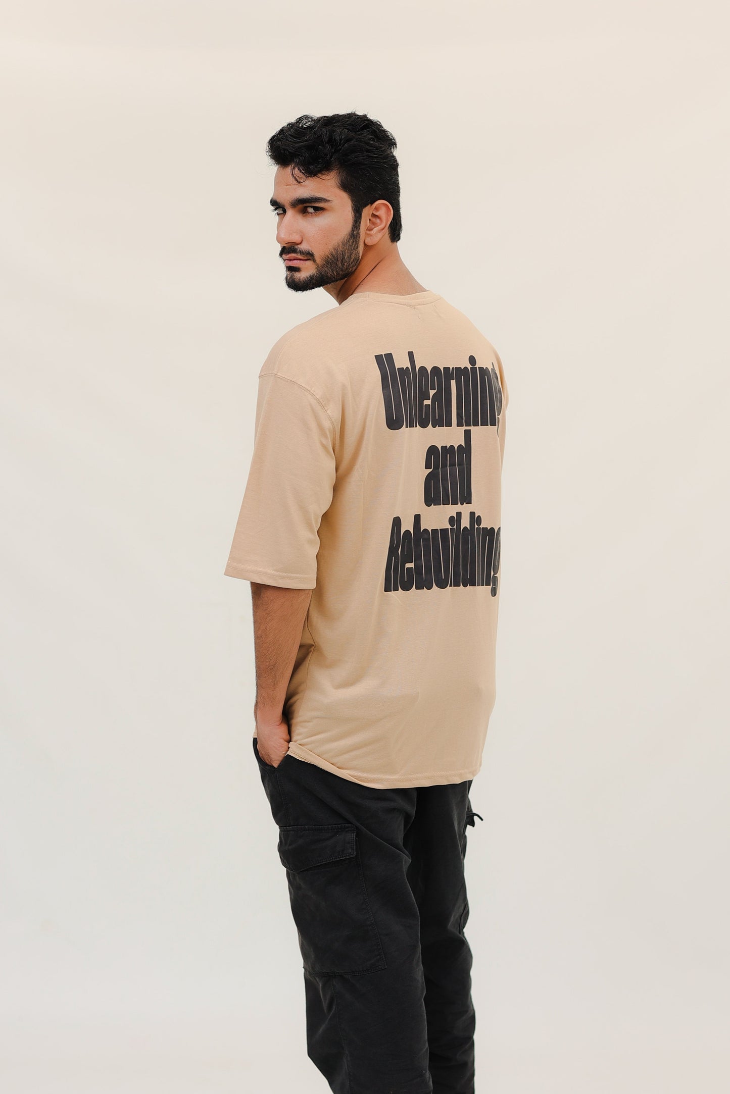 Man wearing a beige t-shirt with text on the back against a white background
