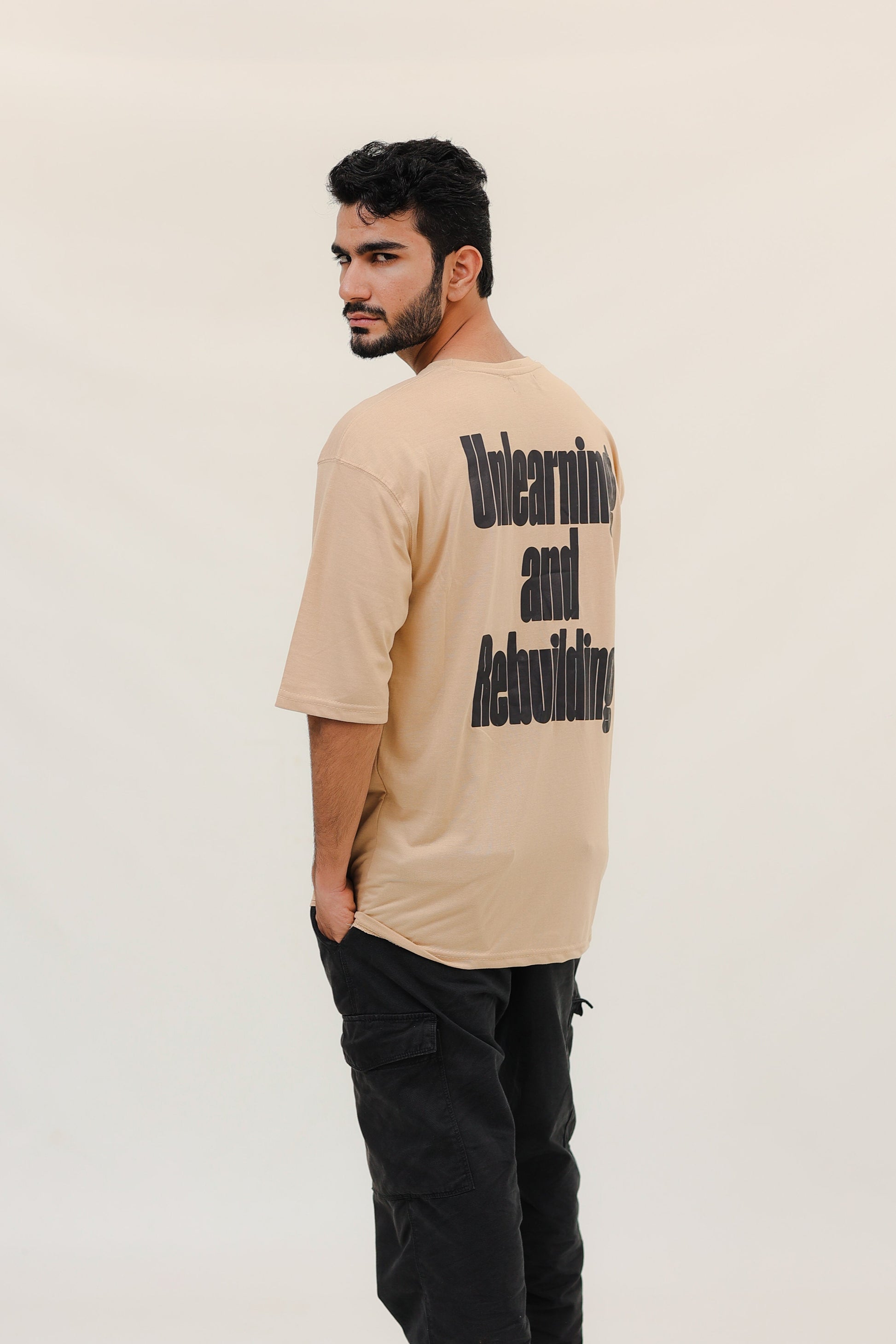 Man wearing a beige t-shirt with text on the back against a white background